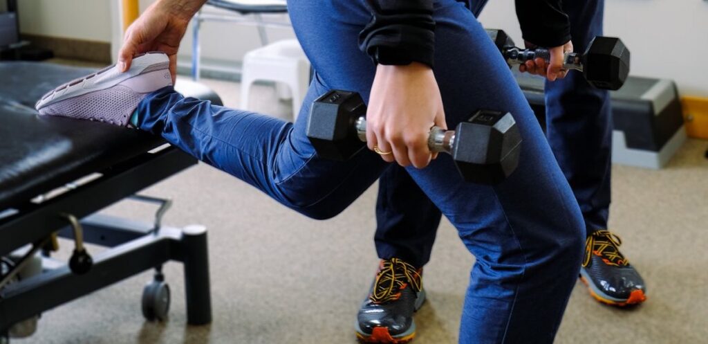 A patient performing a step-up exercise while holding dumbbells during a physiotherapy session